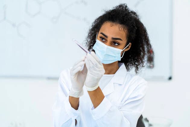 Female researcher examining test tube in laboratory during pandemic model released Symbolfoto property released GIOF11858