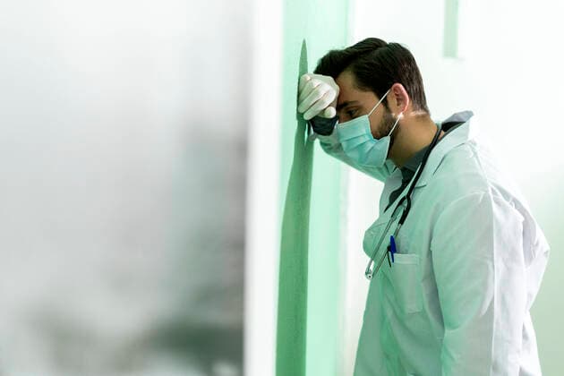 Exhausted male doctor leaning on wall during COVID-19 model released Symbolfoto property released GIOF12260
