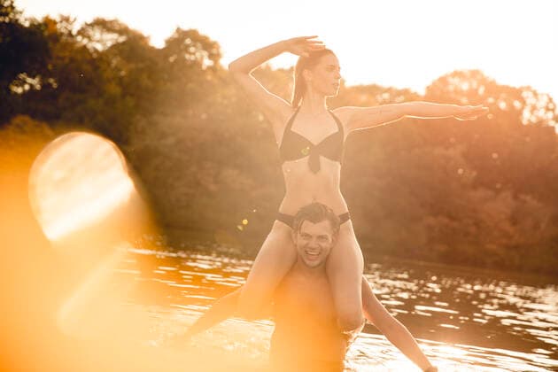 Young woman sitting on shoulders of young man standing in lake, enjoying the sun model released Symbolfoto GUSF02346