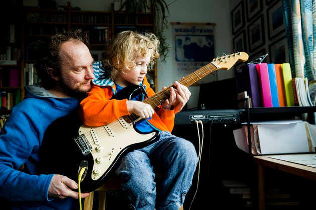 IMAGO Creative: Momentaufnahmen IMAGO Creative: NGO, Ausbildung für Kinder Father teaching electric guitar to blond son while sitting at home model released Symbolfoto property released IHF00439