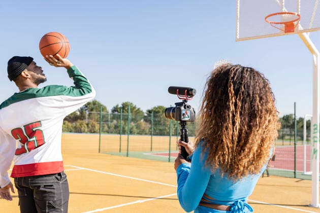 Female filming male friend playing basketball on sports court model released Symbolfoto JCCMF01718