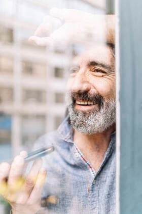 Smiling senior man talking on smart phone at home seen through glass model released Symbolfoto property released JCZF00584