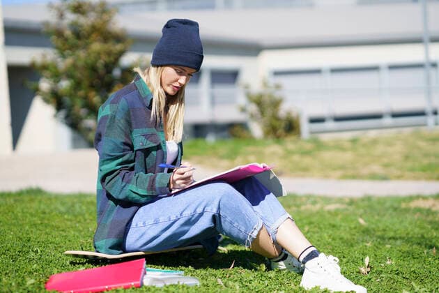 Young woman studying while sitting on skateboard in college campus during sunny day model released Symbolfoto JSMF02097