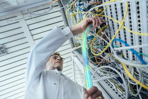 Mature male IT support plugging in fiber optic cable at data center model released Symbolfoto property released LIFIF00013