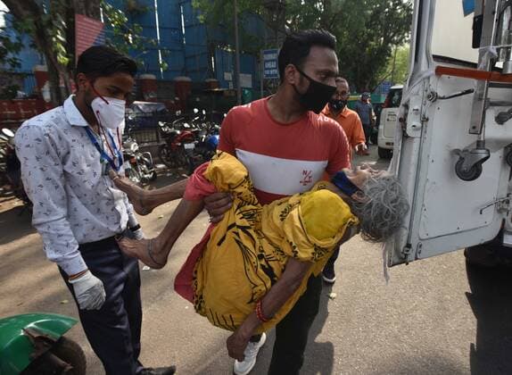NEW DELHI, INDIA - APRIL 27: Patient relatives carry a 80 Year Old lady Chetan Devi from Indira puri Delhi covid patient was ill but hospital dont admit her outside the Lok Nayak Jai Prakash (LNJP) hospital on April 27, 2021 in New Delhi, India. As Covid-19 cases continued to surge in Delhi with over 98,264 active cases people are struggling to get hospital beds, ventilators, oxygen cylinders, injections and medicines with the health infrastructure in the state almost stretched to its limit. (Photo by Sonu Mehta Hindustan Times) As COVID Cases Surge, Indian Hospitals Struggle With Shortage Of Beds