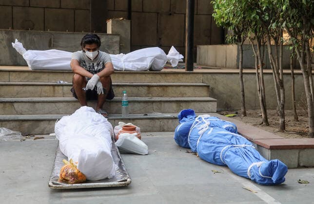 April 28, 2021, New Delhi, India: (EDITORS NOTE: Image depicts death).A man wearing a face mask sits next to the bodies of those who have died from the coronavirus Covid-19 virus for cremation at a crematorium..India faces the world fastest growing number of Covid-19 cases with 360,927 new confirmed infections, the highest single day count in the country and more than 3,293 death in the month of April 2021. New Delhi India - ZUMAs197 20210428_zaa_s197_065 Copyright: xNaveenxSharmax