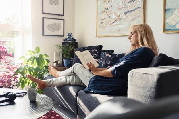 Blond woman reading book while sitting on sofa in living room Sweden, Malmo, model released, property released Copyright: xKentarooxTrymanx , MA86327