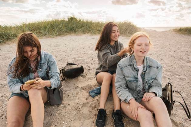 IMAGO Creative, Jahreszeit Sommer, Sommerferien IMAGO Creative: Landleben - Alfresco, Draußen Teenage girl using smart phone while female friends sitting on sand at beach Sweden, Malmo, model released Copyright: xKentarooxTrymanx , MA86376
