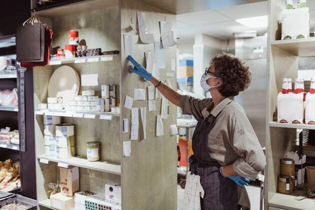 Female owner looking at adhesive notes stick on rack at delicatessen shop during pandemic Sweden, Stockholm, model released, property released Copyright: xMaskotx , MA85946