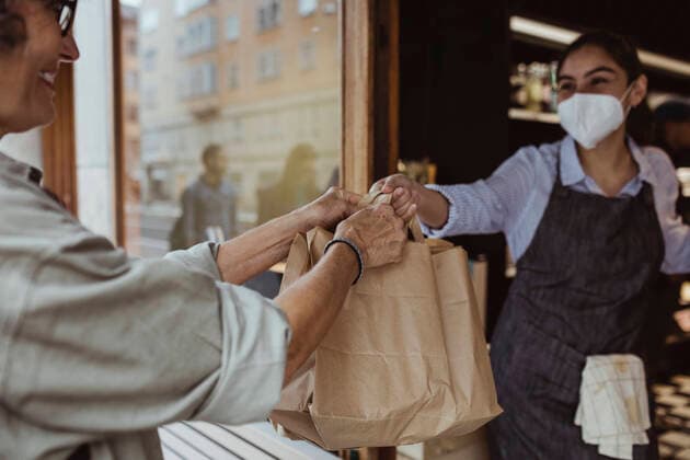 Young sales woman giving take away food to female customer at deli shop during pandemic Sweden, Stockholm, model released, property released Copyright: xMaskotx , MA86000