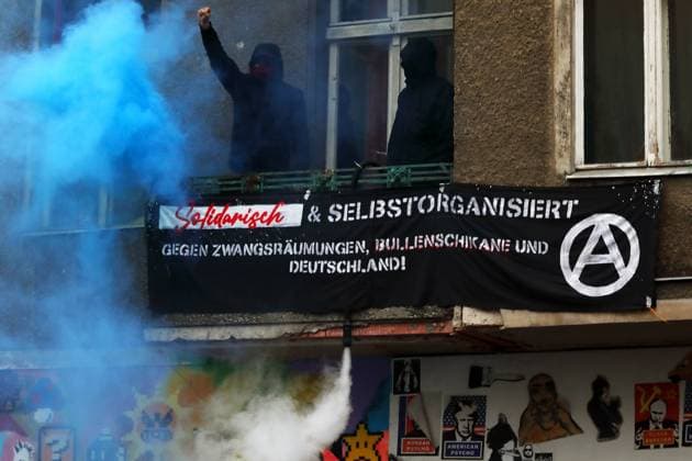 VON DER KRISE ZUR ENTEIGNUNG! - Demonstration für eine soziale und demokratische Lösung der aktuellen Gesundheits- und Wirtschaftskrise - Hunderte protestieren in Berlin auf den Weddinger Straßen zwischen Leopoldplatz und Gesundbrunnen. - Berlin, Deutschland, DEU, GER, 30.04.2021, Berlin-Mitte (Ortsteil Wedding): Zur Demonstration am Vorabend des 1. Mai hat die linke Stadtteilgruppe Hände weg vom WEDDING! aufgerufen, die sich seit 2012 gegen den Ausverkauf des Weddings und andere soziale Missstände organisiert. Aufgrund der Corona-Pandemie tragen die Demonstranten Mundschutz und halten möglichst Abstand zueinander. Protestaktion im selbstverwalteten Hausprojekt der Schererstraße 8: Vermummte Aktivisten auf einem Balkon im blauen D
