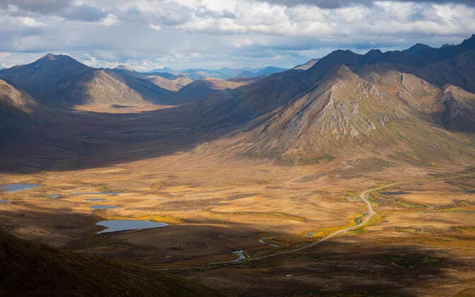 Aerial of majestic mountains with sunlight reflecting over the Dempster Highway under a cloudy sky; Dawson City, Yukon, Canada  Copyright: RobertxJ.xPolett 33343534