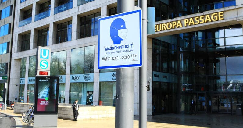 An einem Pfahl vor der Europa Passage in der Hamburger Innenstadt hängt ein Schild, das darauf hinweist, dass in diesem Bereich zu bestimmten Zeiten Maskenpflicht besteht. Altstadt Hamburg