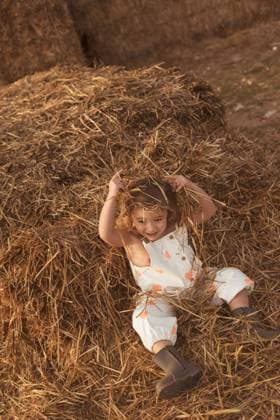 From above cheerful adorable child in overalls playing with hay lying down on straw bales in countryside, Model released Copyright: xAizanex MR