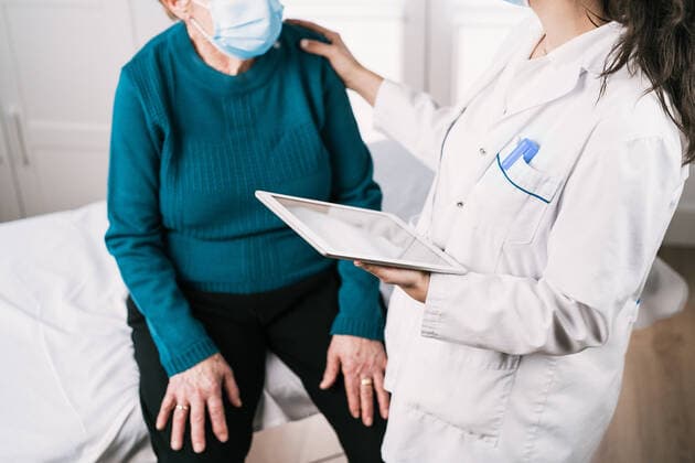 Cropped unrecognizable female medic in uniform with tablet speaking with senior woman in sterile mask on consultation during covid 19 pandemic, Model released, Property released Copyright: xAlvaroxSanchezx MR