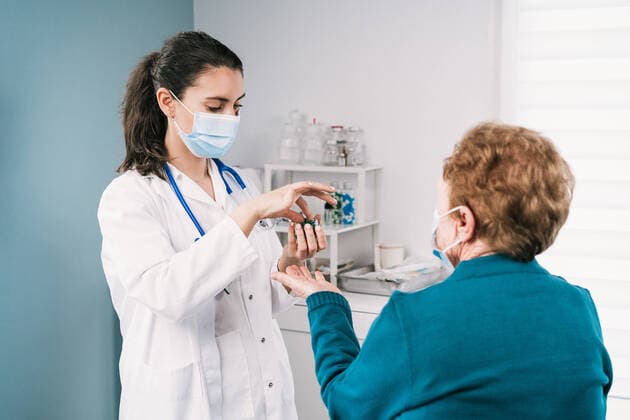 Female medic in uniform and disposable mask preparing medications for anonymous elderly patient on consultation in clinic during pandemic, Model released Copyright: xAlvaroxSanchezx MR