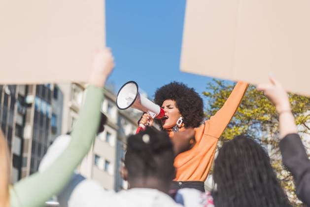 IMAGO Creative: Resilienz IMAGO Creative: Frauenmonat, Feministischer Aktivismus IMAGO Creative: 2022 Aussichten African American female social justice warrior with speaker against crop anonymous multiracial people with placards fighting for human rights in town, Model released Copyright: xIvanxMorenox MR