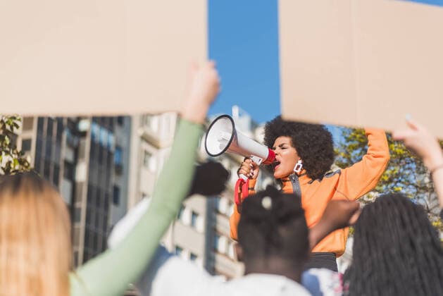 African American female social justice warrior with speaker against crop anonymous multiracial people with placards fighting for human rights in town, Model released Copyright: xIvanxMorenox MR