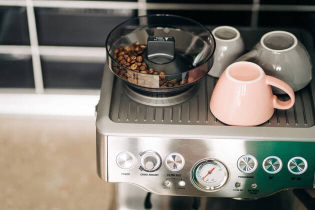 IMAGO Creative: Haushaltsger?te - Kaffeemaschine From above of roasted coffee beans in electric grinder against ceramic cups on rack of modern espresso maker at home Copyright: xJakexJakabx Model Released