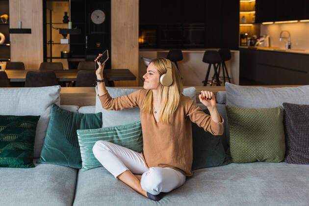 IMAGO Creative: Jahreszeit Winter, Couching Optimistic female sitting on sofa and listening to music in headphones while enjoying songs with raised hands, Model released, Property released Copyright: xJordixMorax MR