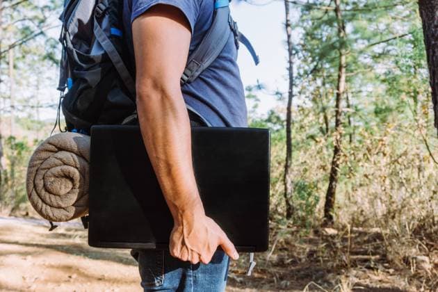 Side view of crop unrecognizable male nomad with belongings standing on footpath with netbook in sunny woods Copyright: xJosexDexJesusxSaldanax Model Released