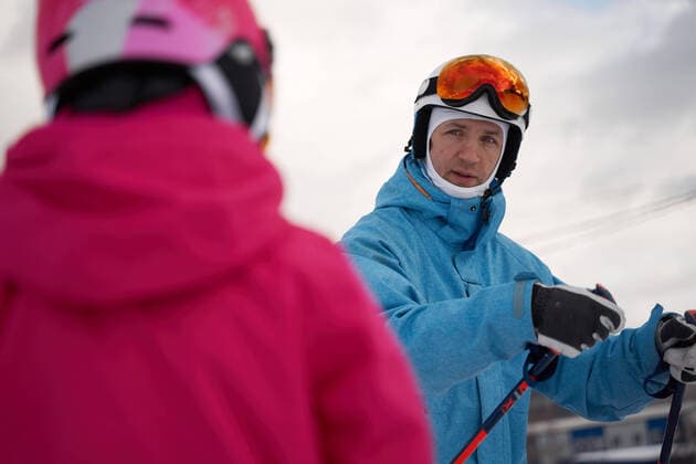 IMAGO Creative: Wintersport, Mode Concentrated parent in warm sportswear and helmet teaching little kid to ski alongside snowy hill slope in winter ski resort, Model released Copyright: xSergeyxMironovx MR