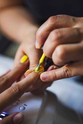 Crop female master applying yellow polish on nails of anonymous client in beauty salon, Model released Copyright: xFrancescxJuanx MR