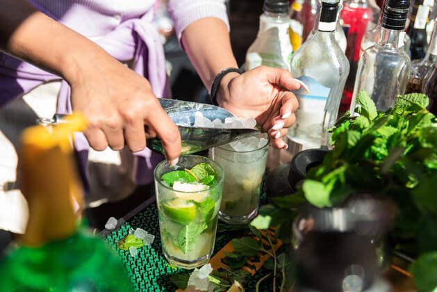 Crop anonymous female barkeeper adding ice cubes into glass while preparing cold refreshing mojito cocktails in sunny outdoor bar, Model released, Property released Copyright: xJulioxRodriguezx MR