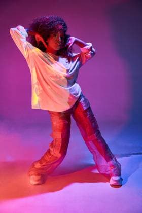 Full length fit young African American female dancer in loose informal wear touching curly hair and looking at camera while dancing in dark studio in neon lights Copyright: xManuelxRuizx Model Released