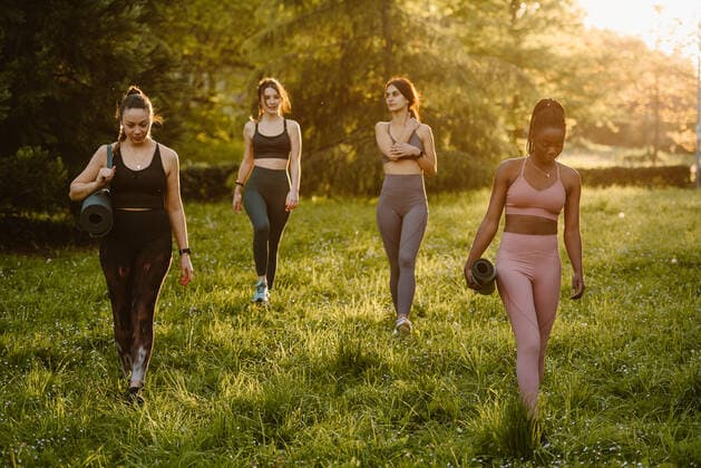 IMAGO Creative: Sommer, Abendspaziergang Confident fit multiracial female athletes walking with mat along lawn during training in summer park in evening, Model released Copyright: xOierxAsox MR