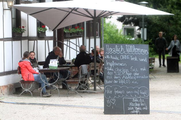 Vor dem Außenbereich eines geöffneten Biergartens in Bad Nauheim befindet sich ein Aufstellernit Aufschrift erzlich willkommen, ab heute ohne Test und Impfausweis. Bitte checken Sie mit der Luca App oder mit dem Adressformular ein, Hessen, Deutschland.