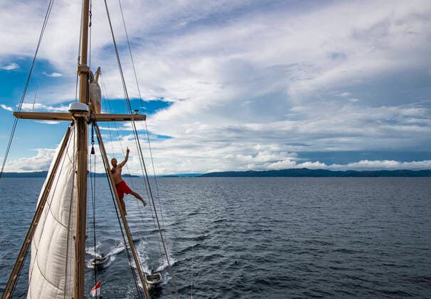 man in board shorts climbing up rigging of sail boat in Raja Ampat Sorong, West Papua, Indonesia CR_THHE210523B-754518-01 ,model released, Symbolfoto ,property released