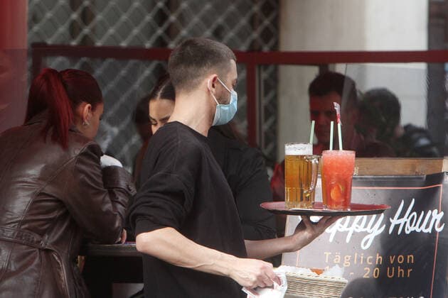 Aufgrund anhaltend niedriger Inzidenzen in Düsseldorf durften gastronomische Betriebe ihren Außenbereich wieder öffnen, sofern Gäste einen negativen Coronatest vorweisen konnten. Ein Kellner mit Maske trägt ein Tablett mit Getränke n an einen der vollbesetzten Tische in einer Bar in der Altstadt, Nordrhein Westfalen, Deutschland