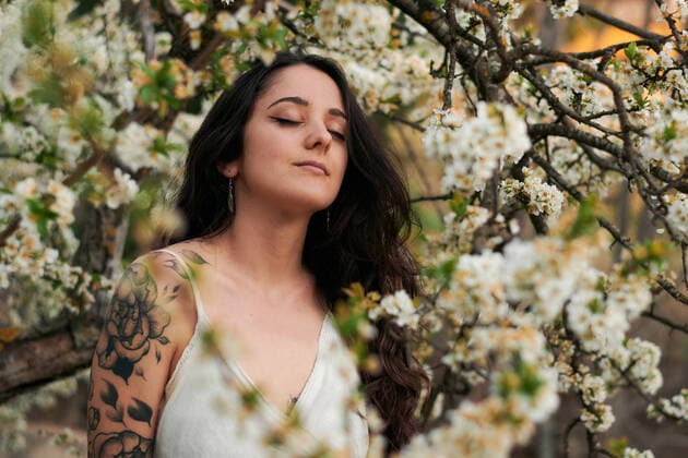 Young female with tattooed arm wearing white dress and standing in flowers of tree with closed eyes, Model released, Property released Copyright: xCristianxBlazquezx MR
