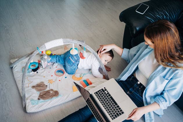 IMAGO Creative: Internationaler Frauentag, Mental Load und Care-Arbeit Top view of mother wearing casual outfit sitting on floor with netbook on laps and outstretching hand to cute little baby playing with toys on floor Copyright: xJakexJakabx Model Released