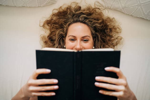 Creative Highlights Symbolbilder From above happy young female with curly hair lying on bed reading book during weekend at home, Model released, Property released Copyright: xJakexJakabx MR
