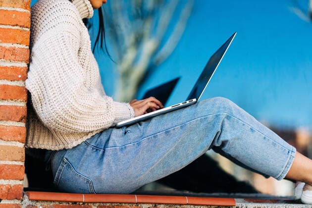 Tschechien, Hochschule streicht wegen KI und Plagiate Bachelorarbeiten Stylish young Asian female remote worker in casual clothes and eyeglasses using laptop while sitting on bench near brick building, Model released Copyright: xJakexJakabx MR
