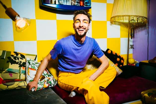 IMAGO Creative: 2023 Farbe des Jahres - Digital Lavender IMAGO Creative: Pride Month, Juni 2022, Pärchen und Familien IMAGO Creative: 2022 Farbe des Jahres: Very Peri, Veilchenblau IMAGO Creative: Clickbait, Modetrends Portrait of cheerful young man sitting on sofa in living room Berlin, Germany, model released, property released Copyright: xMaskotx , MA86653