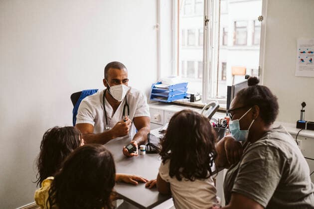 Male doctor talking with woman and girls sitting at desk during COVID-19 Sweden, Stockholm, model released, property released Copyright: xMaskotx , MA86770