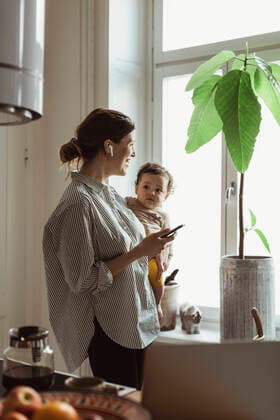 IMAGO Creative: Internationaler Frauentag, Mental Load und Care-Arbeit Businesswoman carrying baby boy while looking through window at home Sweden, Stockholm, model released, property released Copyright: xMaskotx , MA86915