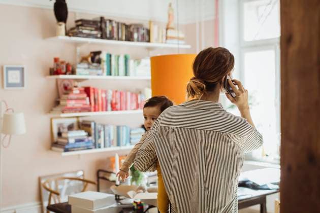 IMAGO Creative: Mutterschaft Rear view of businesswoman carrying baby boy while talking on smart phone at home Sweden, Stockholm, model released, property released Copyright: xMaskotx , MA86923