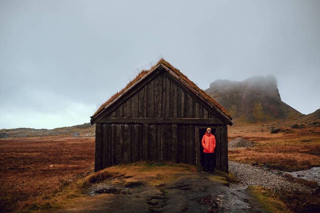 IMAGO Creative: Klimawandel - Nachhaltiges Reisen Young tourist standing near hut between wild lands near high stone hills and cloudy sky, Model released Copyright: xAdrianxSavax MR