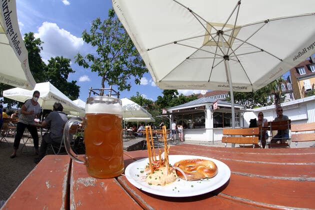 Aufgrund niedriger Inzidenzen in Würzburg durften in Biergärten wieder Gäste im Außenbereich bewirtet werden. Eine Mass Bier und ein Teller mit Obatzda stehen auf dem Tisch eines Biergartens im Sonnenschein, Bayern, Deutschland
