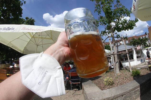 Aufgrund niedriger Inzidenzen in Würzburg durften in Biergärten wieder Gäste im Außenbereich bewirtet werden. Eine Hand mit FFP-2 Maske am Handgelenk hält eine Mass Bier im Sonnenschein hoch, Bayern, Deutschland