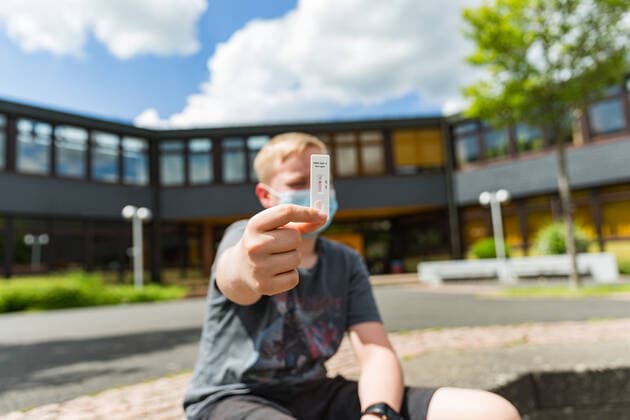 04.6.2021, Corona-Selbsttestpflicht gilt auch nach den Pfingstferien Auch nach den Pfingstferien gilt in Bayern eine Inzidenzunabhängige Testpflicht für alle Schülerinnen und Schüler. Zwei Selbsttests müssen die Kinder auch weiterhin je Woche über sich ergehen lassen. Hier ein Junge, der vor einer Schule sitzt und an sich einen Selbsttest der Marke AESKU.RAPID SARS-CoV-2 Rapid Test von Aldi durchführt. Bad Brueckenau Gesamtschule Bayern Deutschland