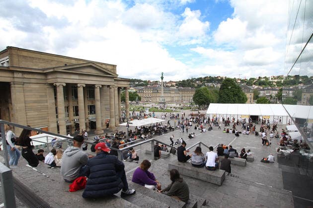 Personen sitzen entspannt auf den Stufen der Freitreppe am Schlossplatz in der Innenstadt von Stuttgart, Baden Württemberg, Deutschland