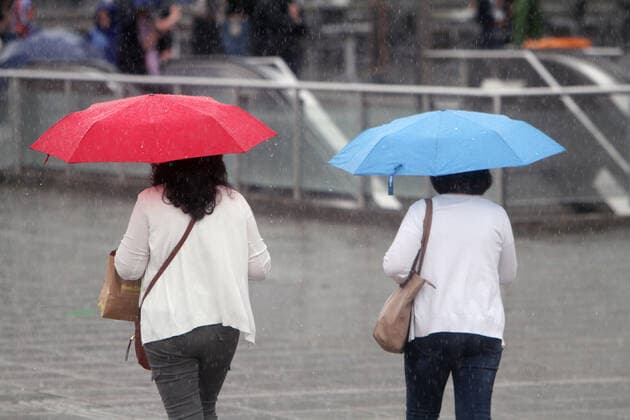 Zwei Frauen gehen mit farbenfrohen Regenschirmen über den Schlossplatz in der Innenstadt von Stuttgart während eines starken Regenschauers, Baden Württemberg, Deutschland