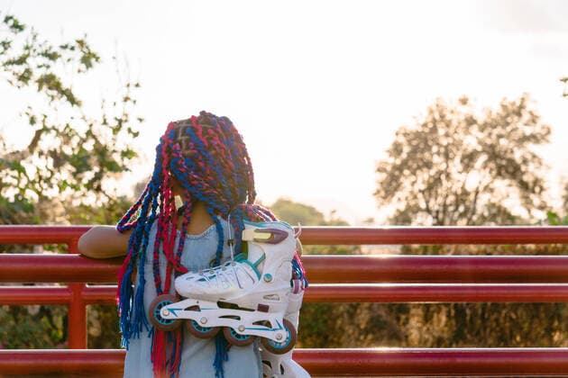IMAGO Creative: Lokalhelden - Jugendsportbildung Back view of anonymous Mexican kid with colorful braids admiring trees while leaning on fence in evening Copyright: xJosexDexJesusxSaldanax Model Released