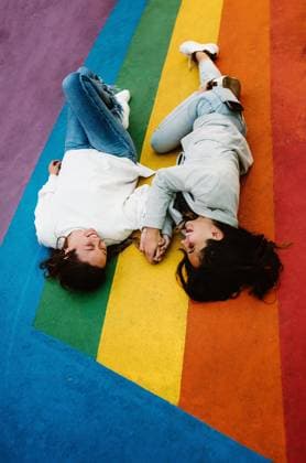 From above cheerful young homosexual girlfriends lying close on rainbow colored floor and having fun, Model released Copyright: xOierxAsox MR