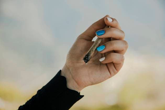 Young woman holding burning marijuana cigarette in hand model released Symbolfoto ACPF01232